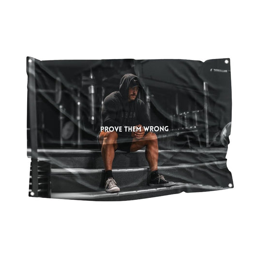 Motivational CBUM gym flag featuring a focused athlete in a hoodie with the phrase "PROVE THEM WRONG" in a gritty workout environment