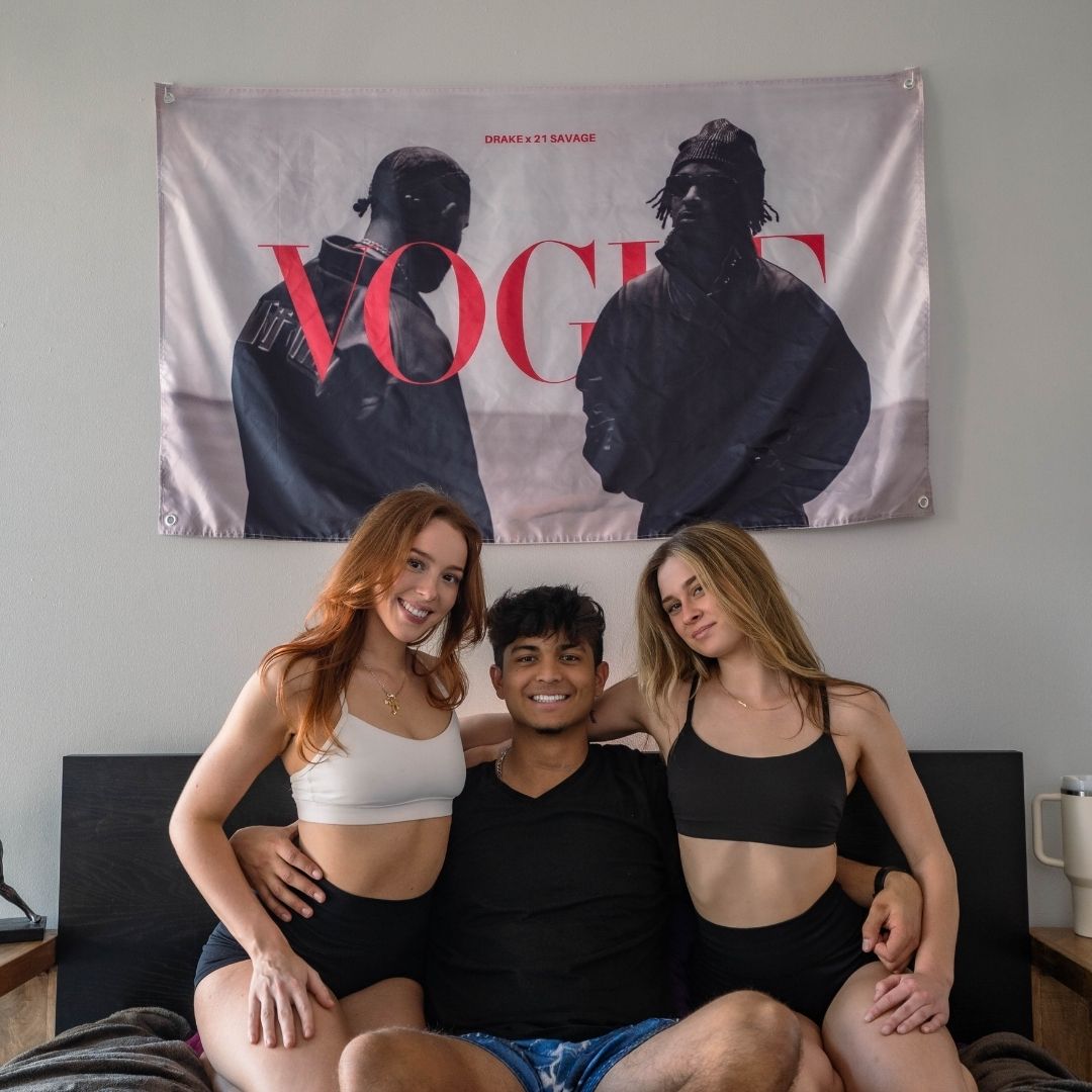 Image of a wall-hanging flag with Drake and 21 Savage in monochrome behind three people posing playfully in casual clothing.