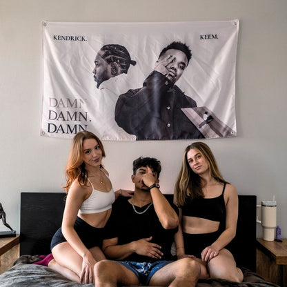 Friends enjoying a moment in front of a black and white flag of Kendrick Lamar and Baby Keem.