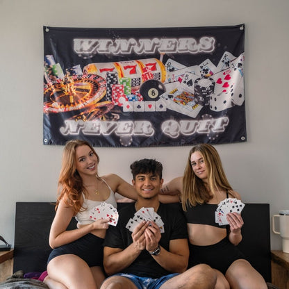 Three friends holding playing cards in front of a wall flag with a vibrant casino gambling design