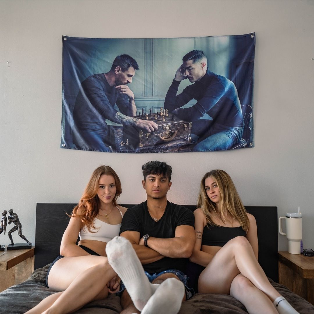 Group of friends with a wall flag depicting messi and ronaldo ina focused chess match, adding a sophisticated touch to a casual room.