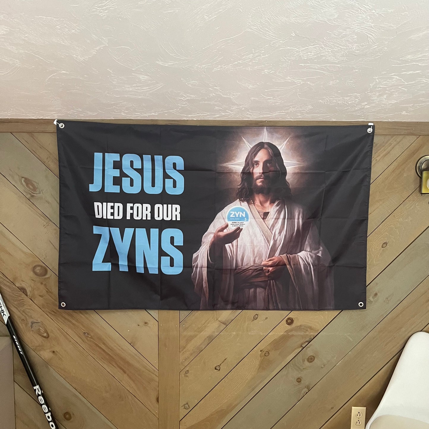 Jesus Zyn flag displayed in a modern room, emphasizing the humorous and bold design of Jesus holding a Zyn pouch with the text "Jesus Died For Our Zyns," ideal for adding a fun and irreverent touch to any space.