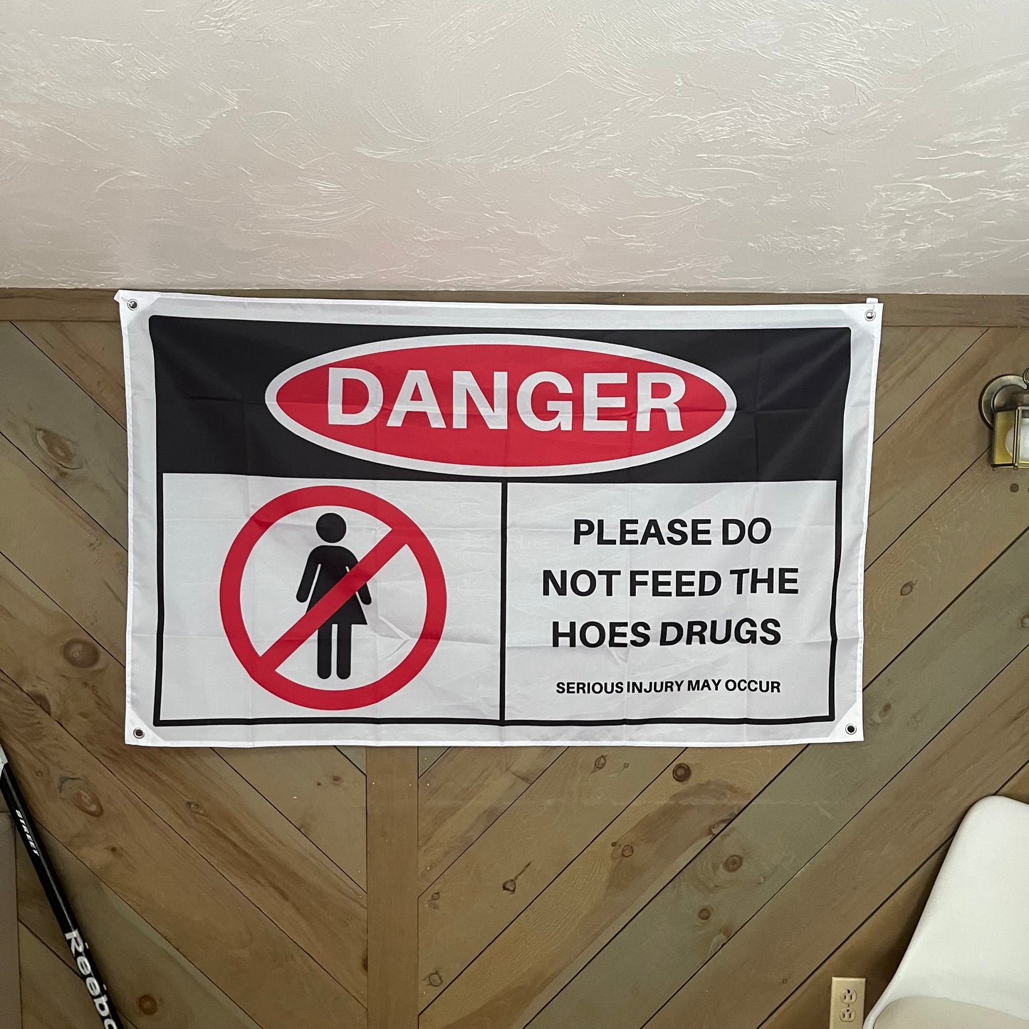 "Danger: Please Do Not Feed the Hoes Drugs" flag displayed in a stylish room, adding a humorous and edgy element to the decor, perfect for college dorms and party setups.