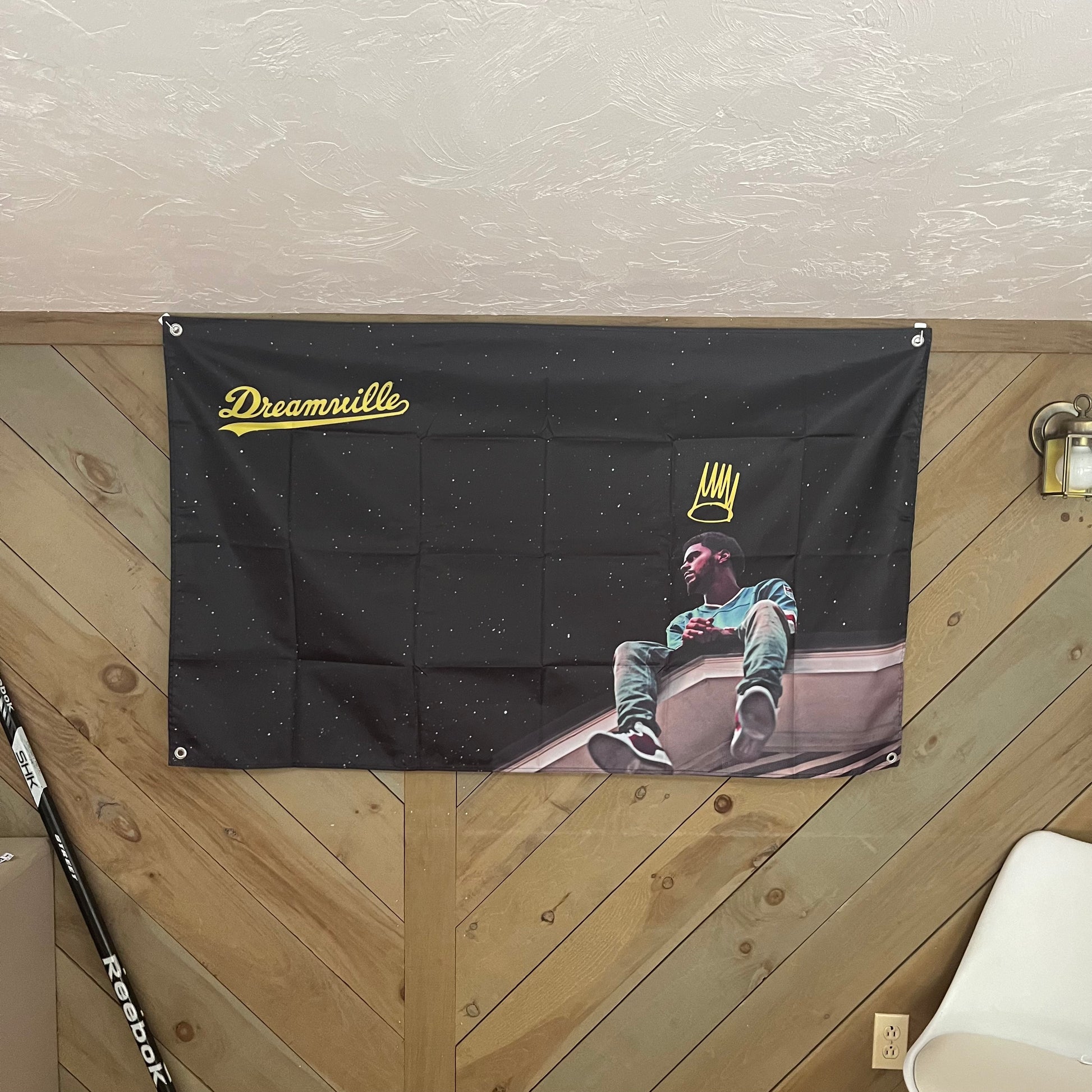 J. Cole Dreamville flag displayed in a modern room, emphasizing the vibrant colors and detailed design of the artist sitting under a starry sky, perfect for music fans and contemporary decor.